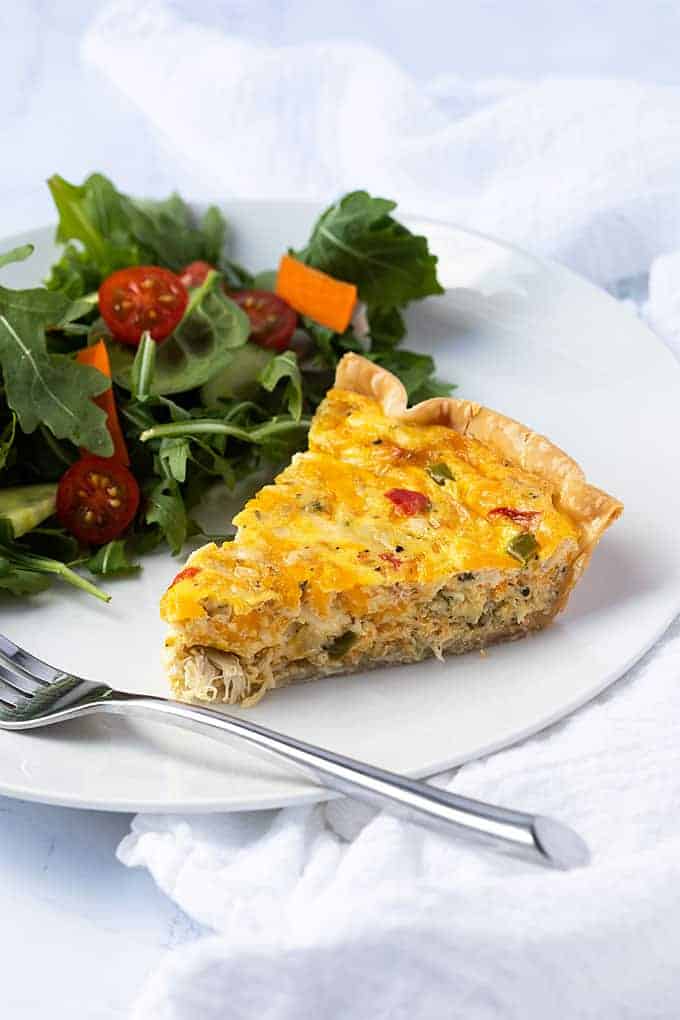 A slice of crab quiche and a garden salad on a white plate with a fork.