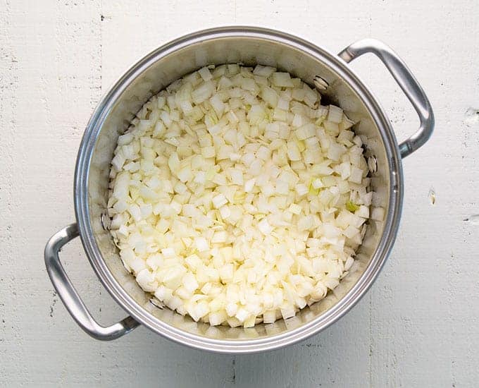 Overhead view of chopped onions over a layer of potatoes in a stainless pot.