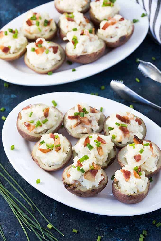 Baby red potato poppers on two white plates beside a pair of tongs.