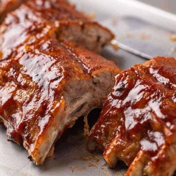 Baked sliced baby back pork ribs on a baking sheet with a knife in the background