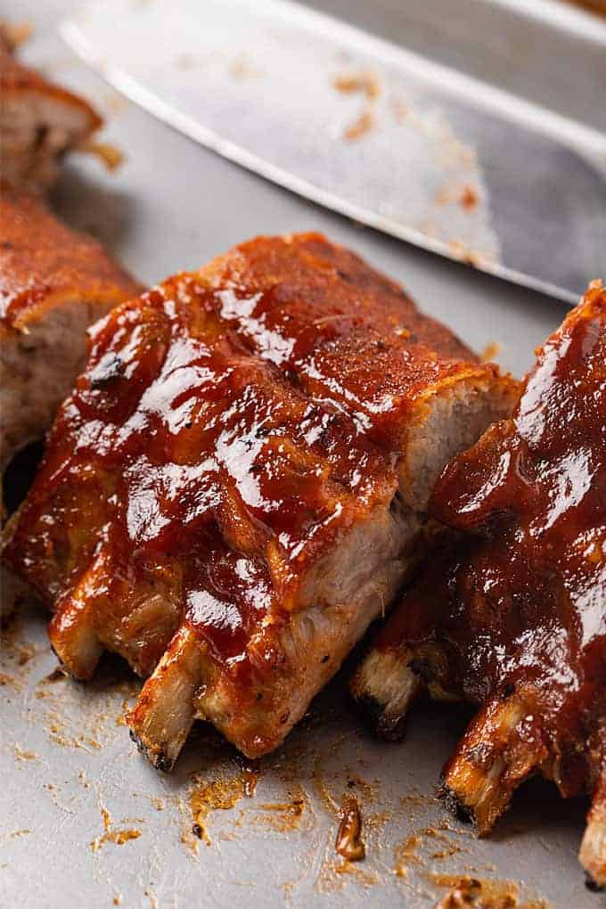 Sliced baby back pork ribs brushed with barbecue sauce on a baking sheet.