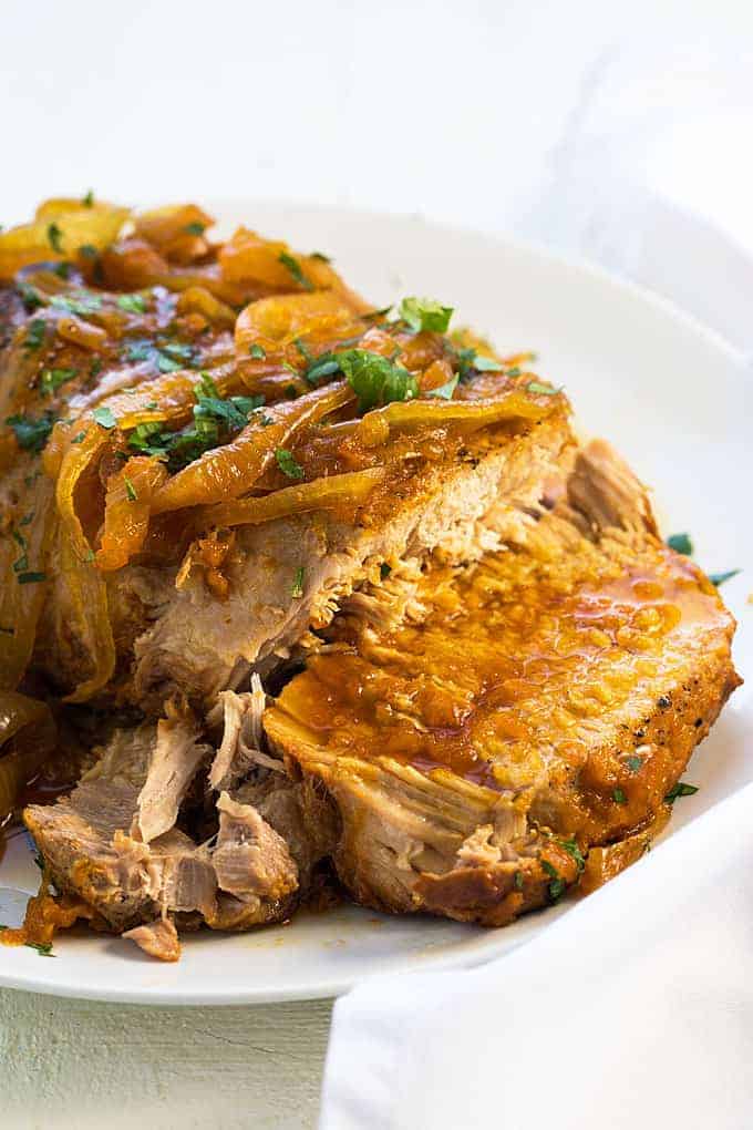 A sliced pork roast topped with onions and apricot glaze on a white platter.