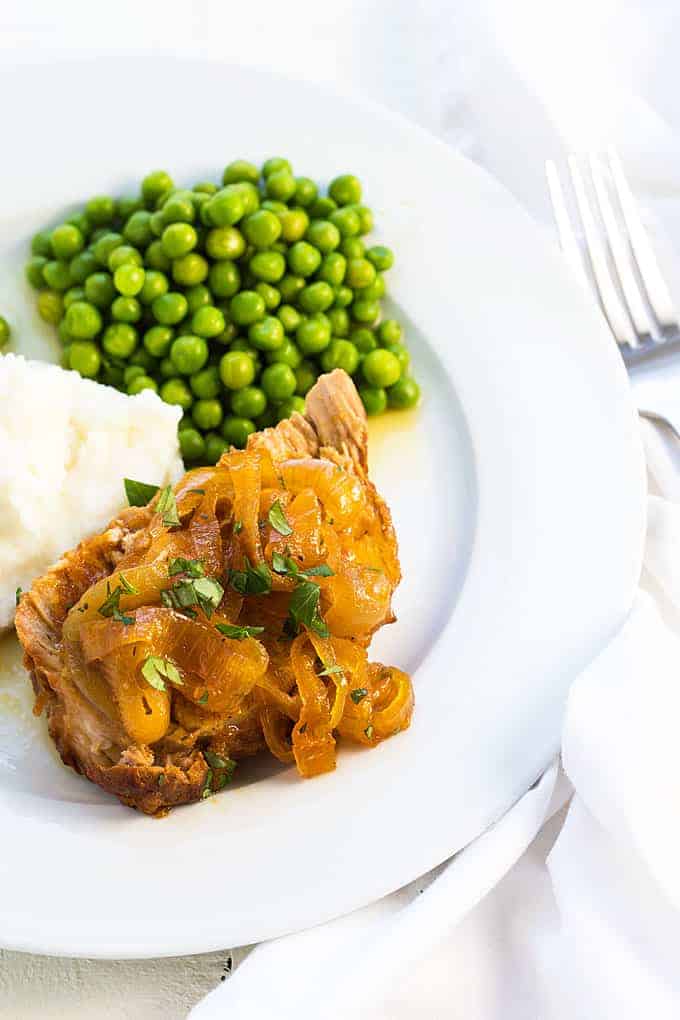 A slice of apricot pork roast, green peas and mashed potatoes on a white plate.  
