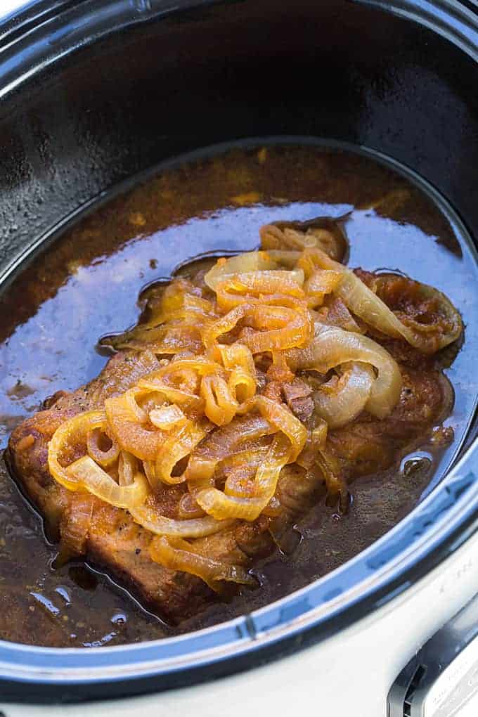 A cooked pork roast topped with onions in a slow cooker.