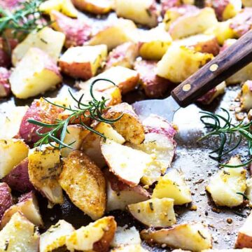 Roasted chopped potatoes with rosemary on a baking sheet with a spatula.