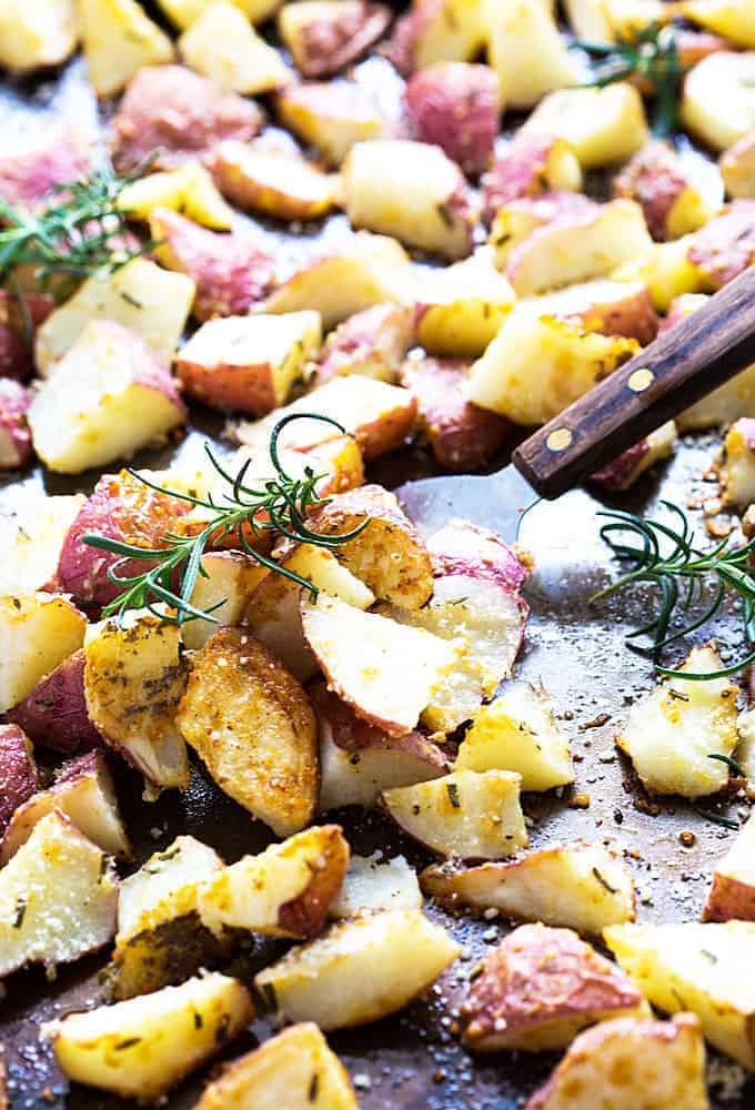 Roasted chopped potatoes with rosemary on a baking sheet with a spatula.