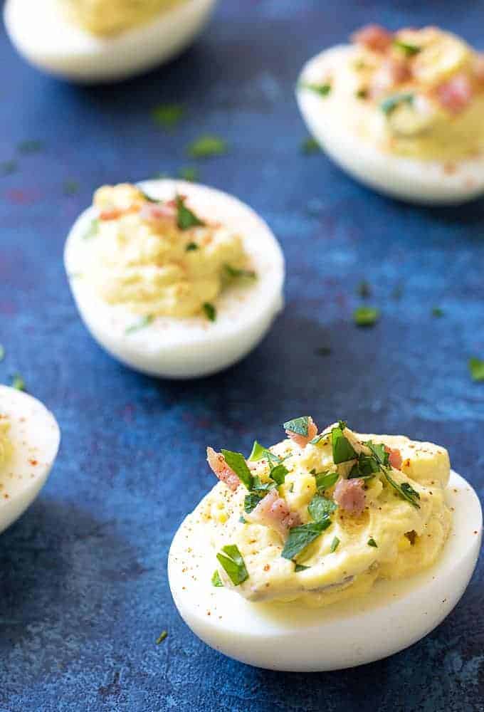 Front closeup view of a deviled egg prepared with bacon and horseradish on a blue surface.