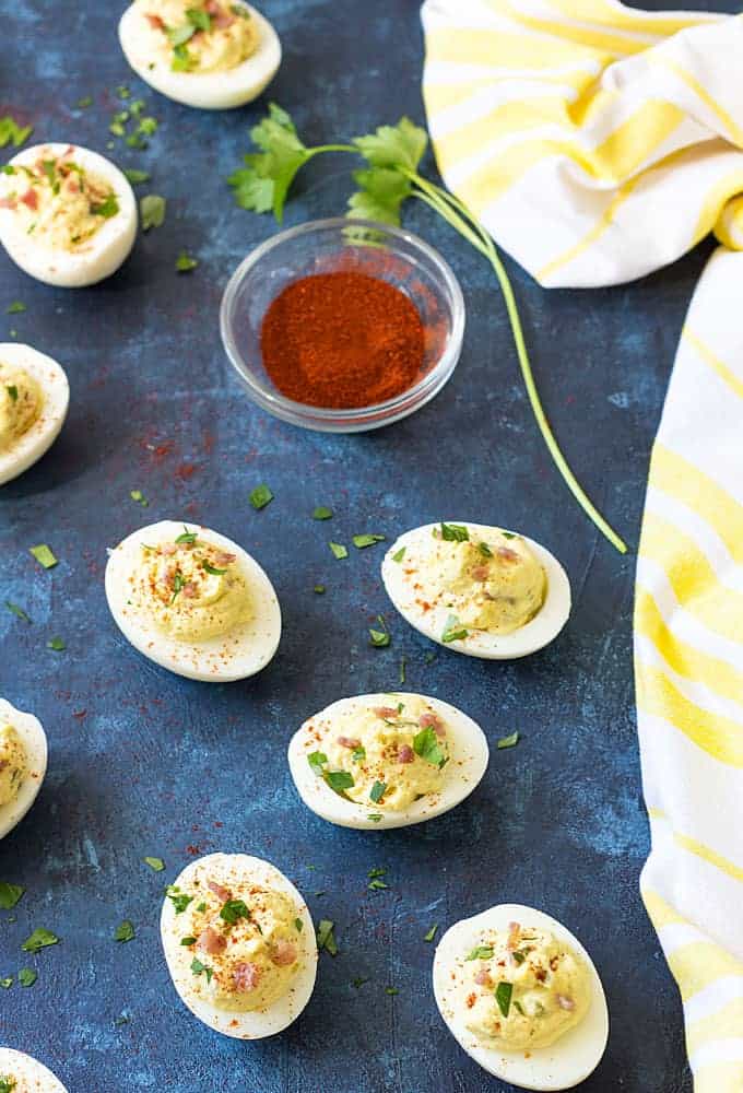 Overhead view of deviled eggs on a blue surface with a small bowl of paprika.