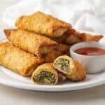 Collard green egg rolls on a white plate with chili sauce