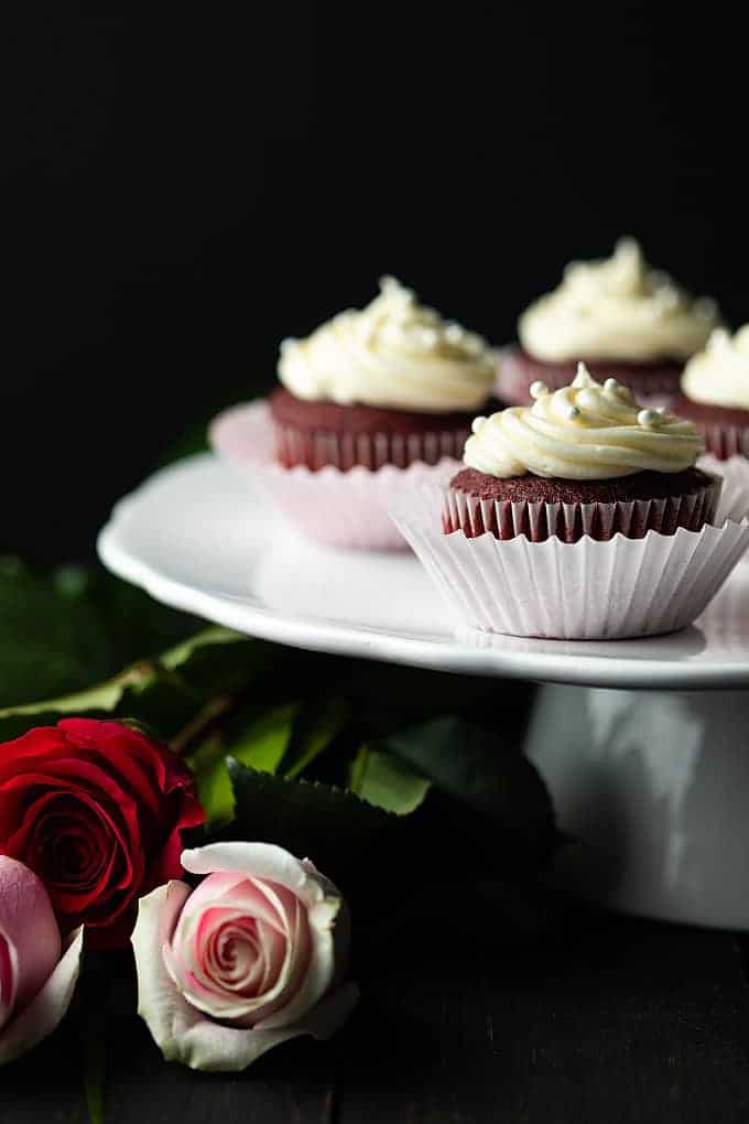 Red Velvet Cupcakes with cream cheese frosting on a cake stand with long-stemmed red and pink roses.