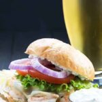 Front view of a shrimp burger with a glass of beer in the background.