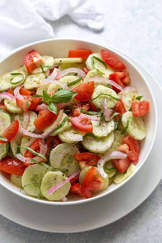Overhead view of cucumber tomato salad in a round white serving bowl.