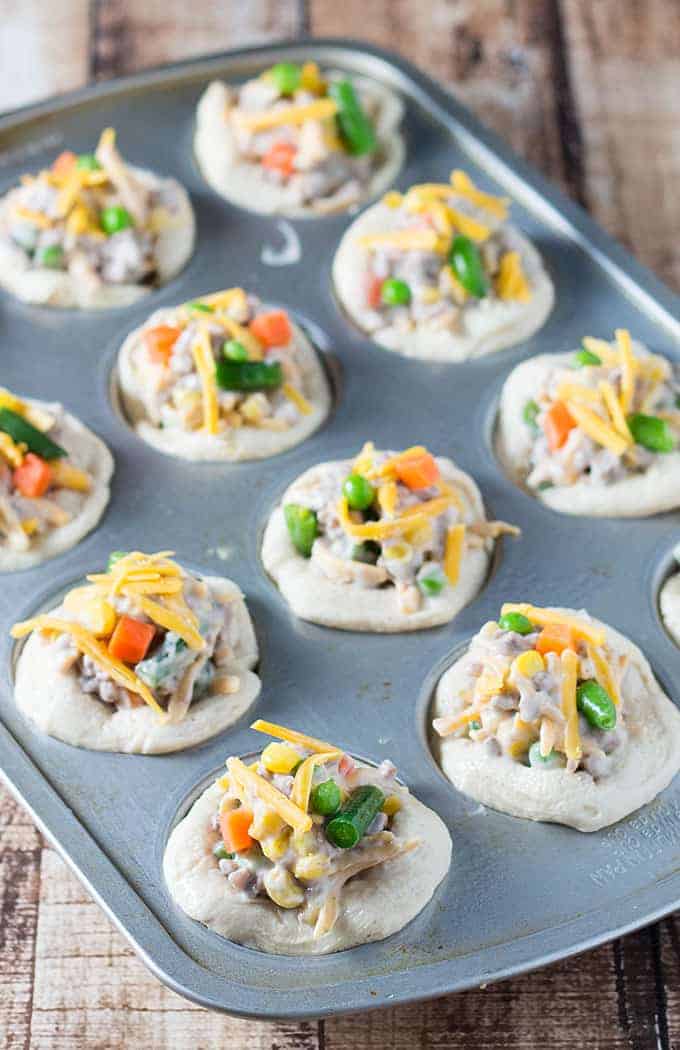 Unbaked biscuits in a muffin pan topped with a beef and vegetable mixture and cheese.