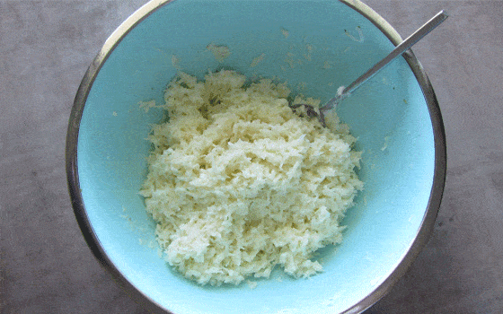 Coconut macaroon mixture in a blue bowl with a spoon.