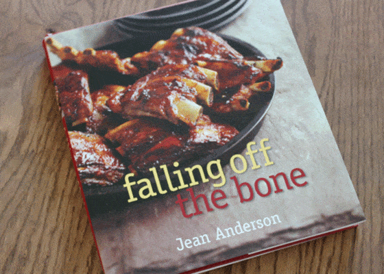 A cookbook with a photo of barbecue ribs on the cover on a wooden surface.