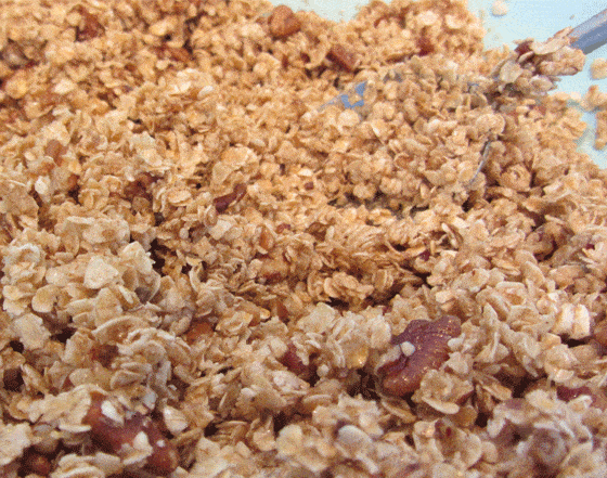 A closeup of granola with a spatula on a baking sheet.