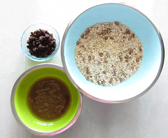 A glass bowl of raisins, blue bowl with oat mixture and green bowl with honey mixture. 