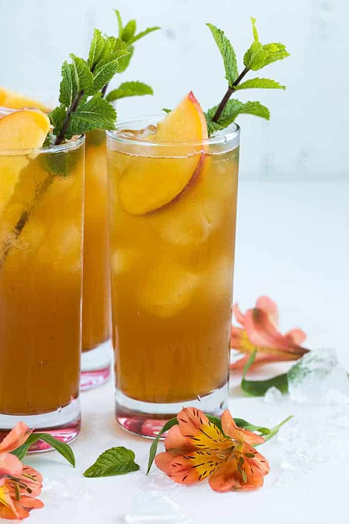 Front view of three glasses of spiked peach tea garnished with peaches and mint.