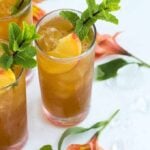 Three glasses of peach tea whiskey cocktail garnished with sliced peaches and mint.