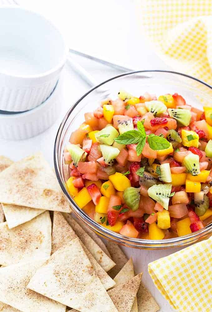 Overhead view of a bowl of tropical fruit salsa beside cinnamon chips and a napkin.