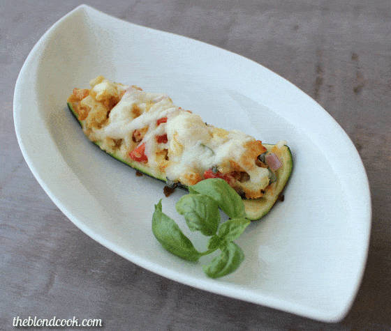 A zucchini boat beside a sprig of fresh basil on a white plate.