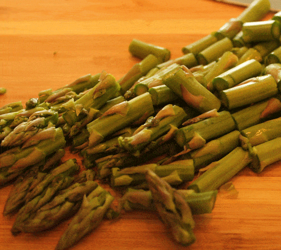 Fresh asparagus spears that have been cut into pieces on a cutting board.