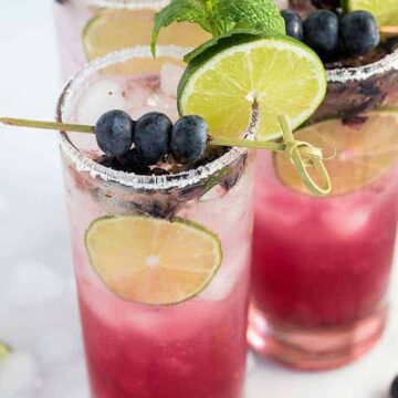 Three blueberry mojitos garnished with blueberries, lime and mint.