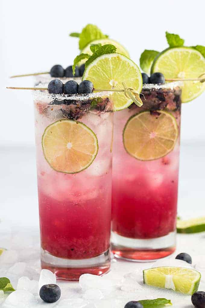 Front view of three garnished blueberry mojito cocktails on a white background.
