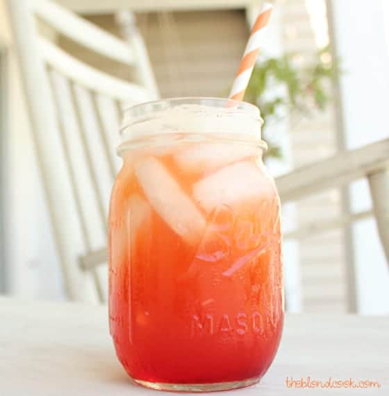 An orange cocktail in a mason jar with a straw.  A rocking chair is in the background.