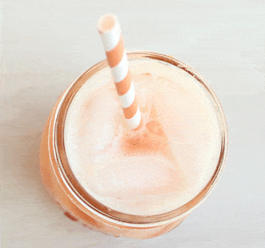 Overhead view of an orange cocktail with ice in a glass with a straw.