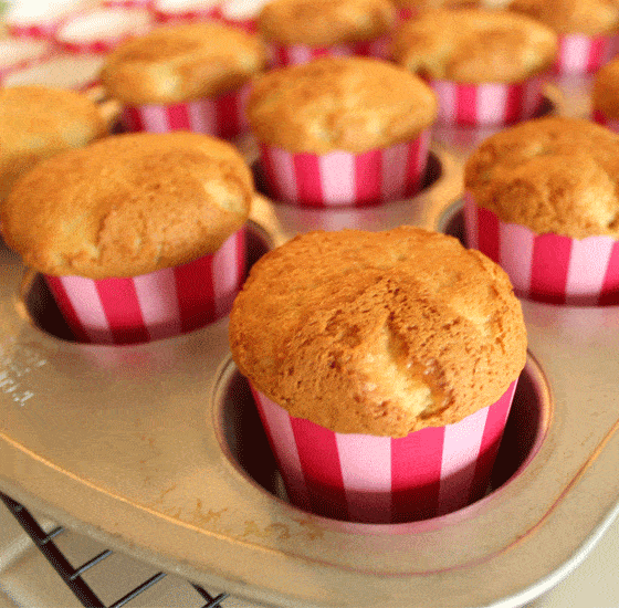 Closeup of freshly baked cupcakes in pink striped liners in a muffin pan.