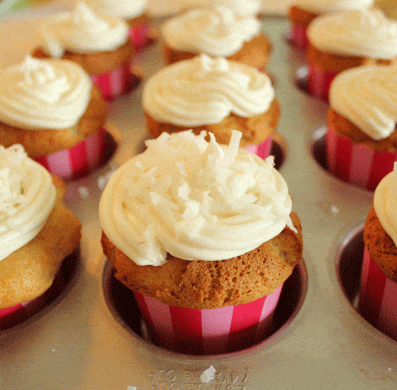 Cupcakes in pink striped liners with white frosting sprinkled with coconut.