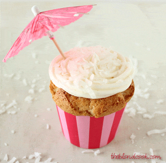 Cupcakes in a pink striped cupcake liner with white frosting and a pink umbrella.