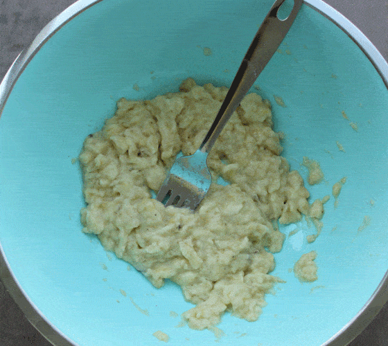 Overhead view of mashed bananas in a blue bowl with a fork.