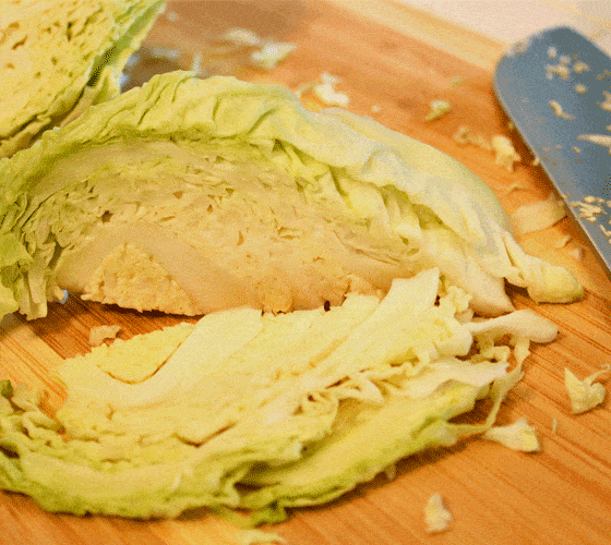 Sliced cabbage beside a knife on a wooden cutting board