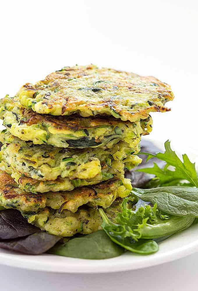 A stack of zucchini fritters with mixed greens on a white plate.