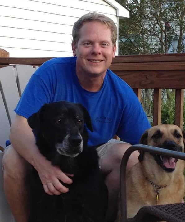A man in his early forties with light brown hair wearing a blue shirt with two dogs.