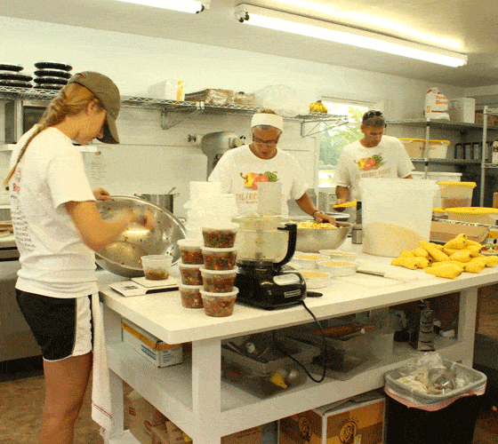 Three employees wearing white t shirts working in a kitchen at a large white table.