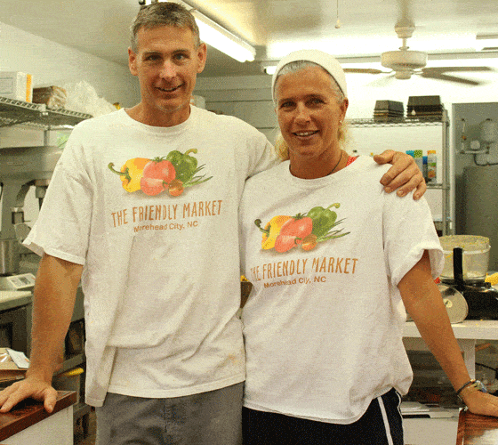 A married couple with white t shirts standing in a kitchen smiling.  The man has his arm around his wife.