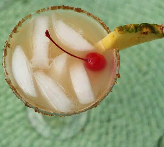 Overhead view of a pineapple cocktail with ice in a glass rimmed with brown sugar.