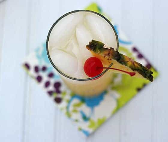 Overhead view of a pineapple cocktail garnished with fresh pineapple and a cherry.