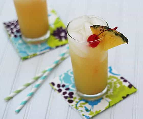A pineapple cocktail in a glass on a patterned napkin by 2 straws.