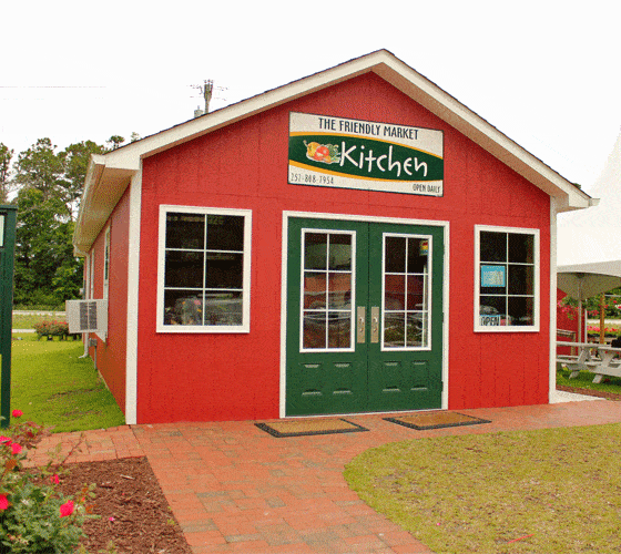 A small red wooden building with green doors and a brick walkway.