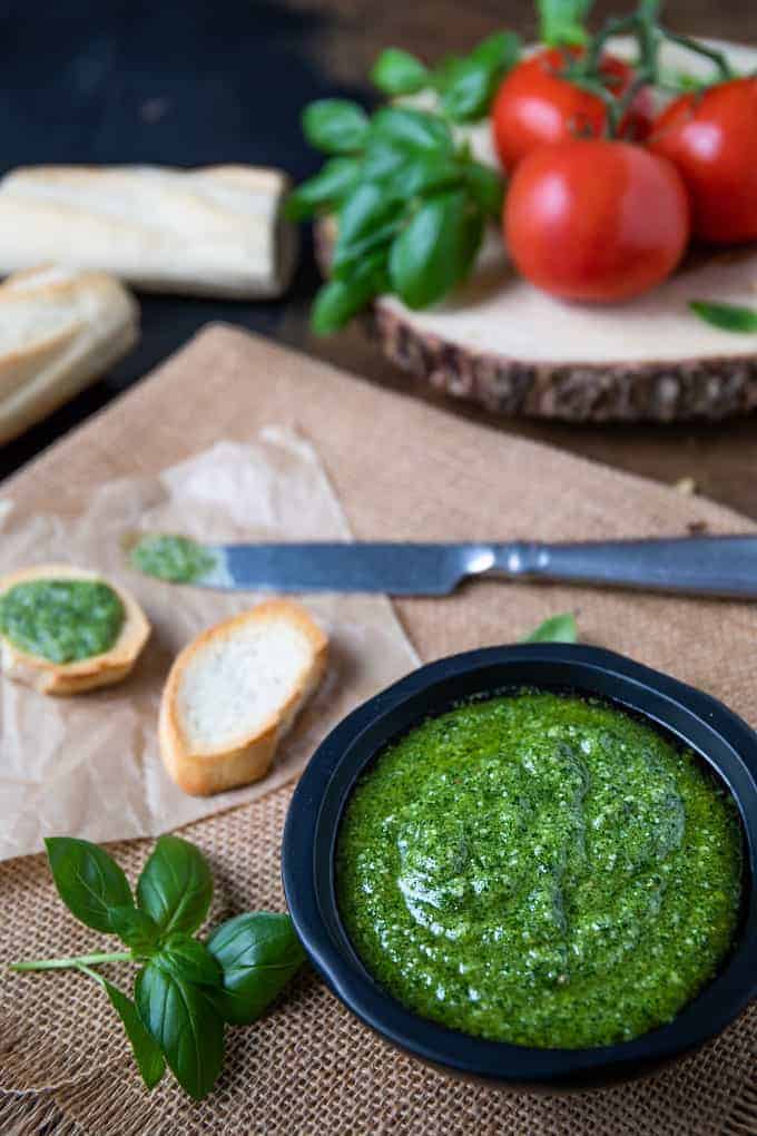 Basil pesto in a black bowl with French bread, fresh tomatoes and basil leaves.