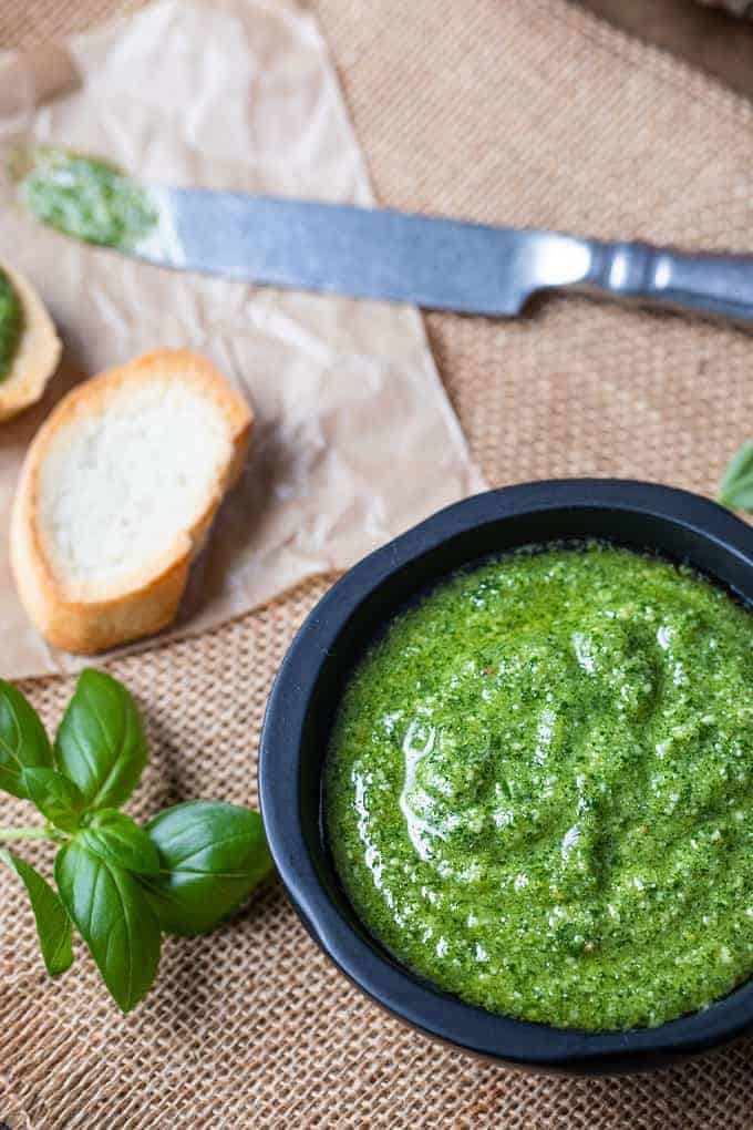 Basil pesto in a black bowl with French bread, fresh tomatoes and basil leaves.