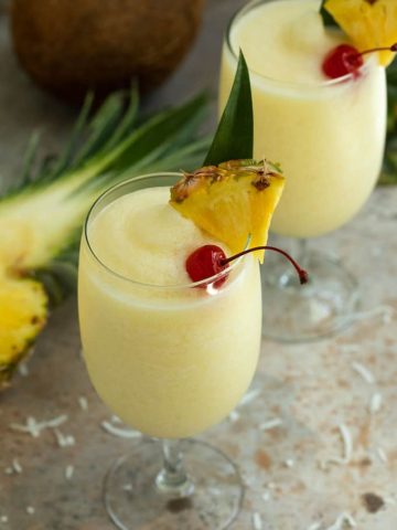 2 glasses of pina colada cocktail garnished with maraschino cherries and pineapple wedges