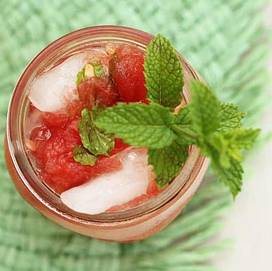 Overhead closeup view of a watermelon cocktail in a jar garnished with fresh mint.