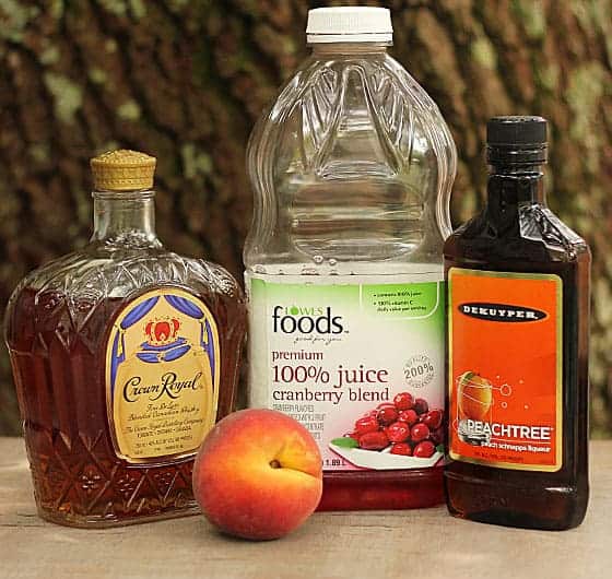 Bottles of whiskey, cranberry juice, peach schnapps and a fresh peach.