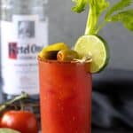 A garnished bloody Mary cocktail.  A bottle of vodka is in the background.