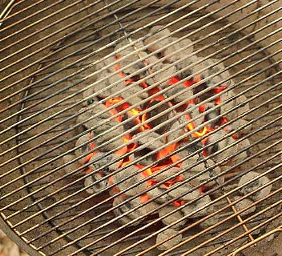 Overhead view of coals burning under a grate in a round charcoal grill.